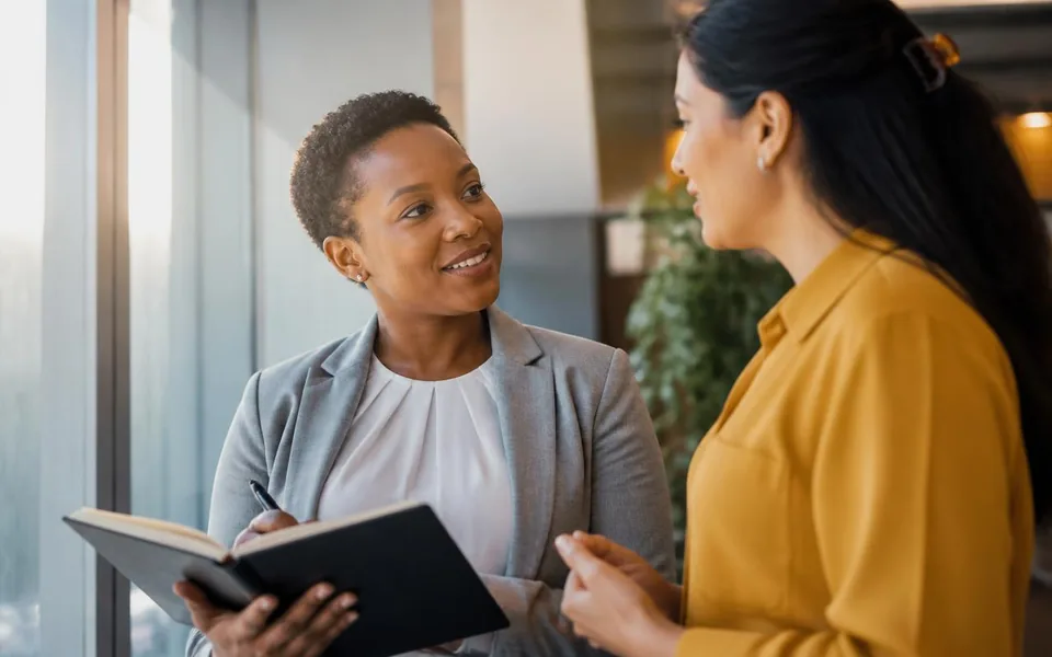 Two clinical research professionals in a career conversation beside an office window.